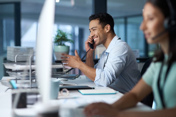 Shot of a young man answering the phone while working in a modern call centre