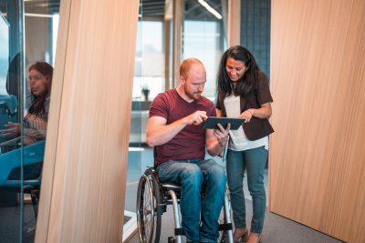 Young Man in a Wheelchair and Mature Woman Using Digital Tablet