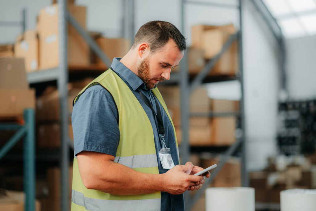 Warehouse, worker and ecommerce businessman with checklist on phone in logistics, shipping or online shopping factory. Supply chain, retail and cargo delivery man in export, package or courier plant