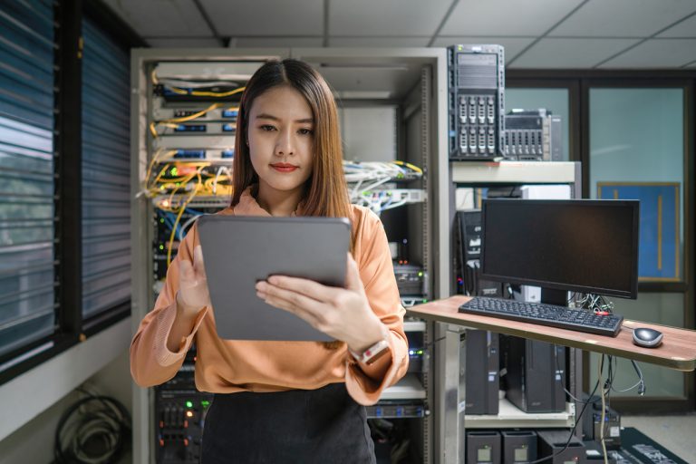 Technician holding digital tablet while examining server in server room
